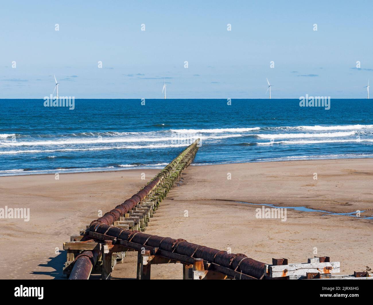 Outfall pipe at Cambois, Northumberland, UK into blue sea with wind turbines in the distance. Stock Photo