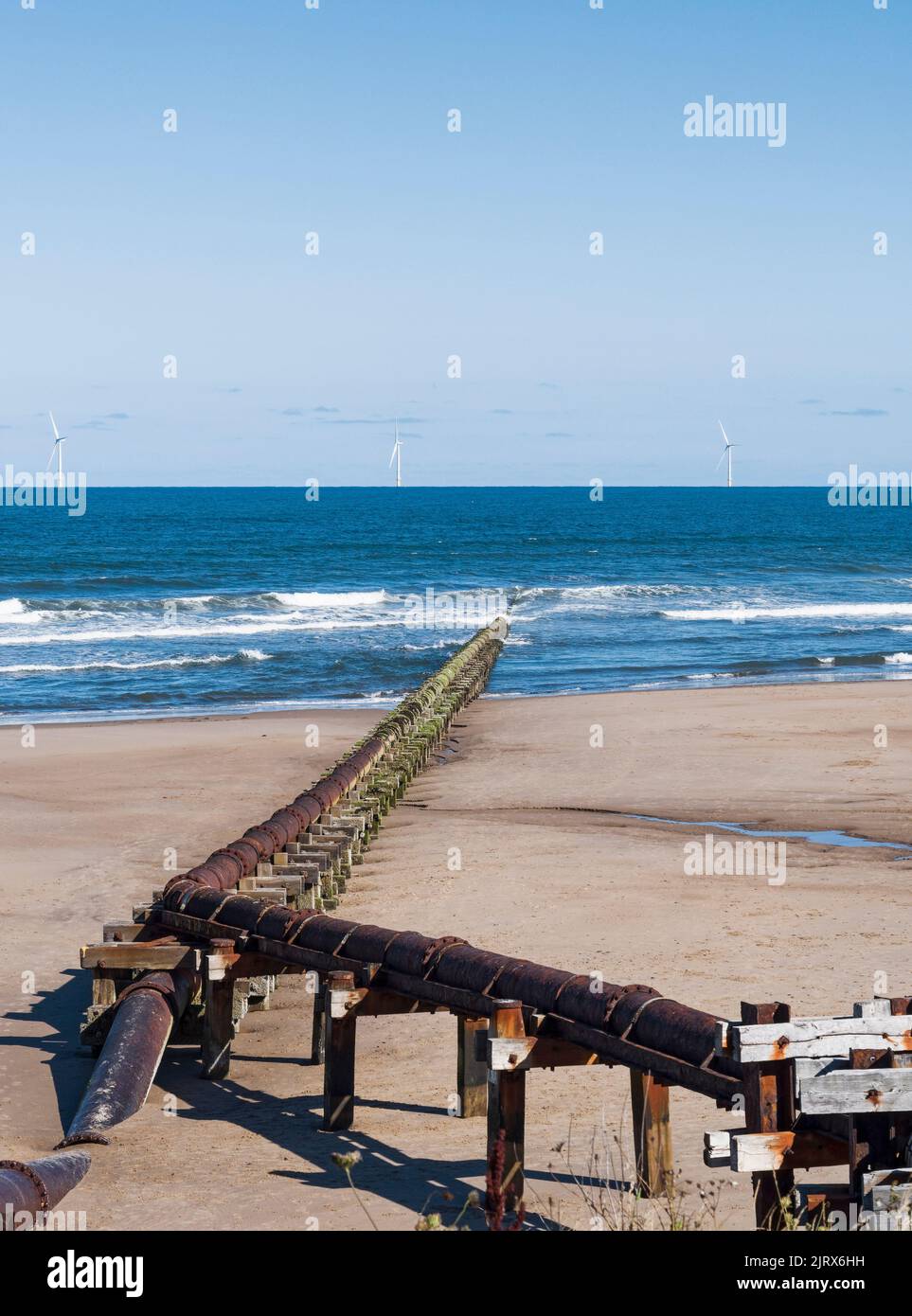 Outfall pipe at Cambois, Northumberland, UK into blue sea with wind turbines in the distance. Stock Photo