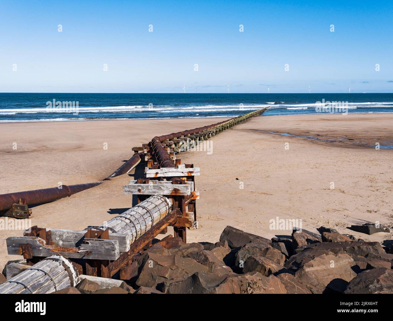 Outfall pipe at Cambois, Northumberland, UK into blue sea with wind turbines in the distance. Stock Photo