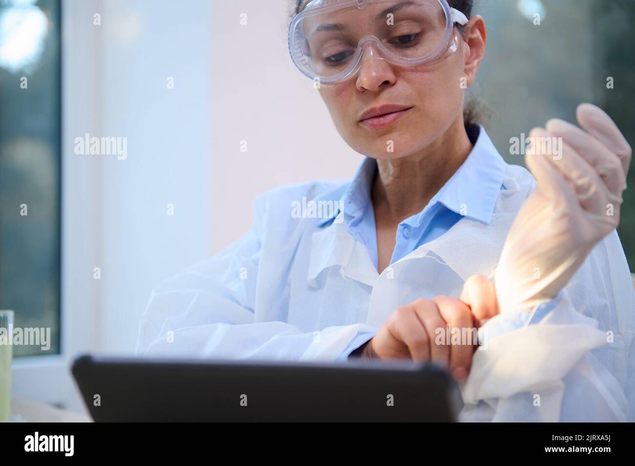Closeup female scientist in white lab coat and safety goggles works on