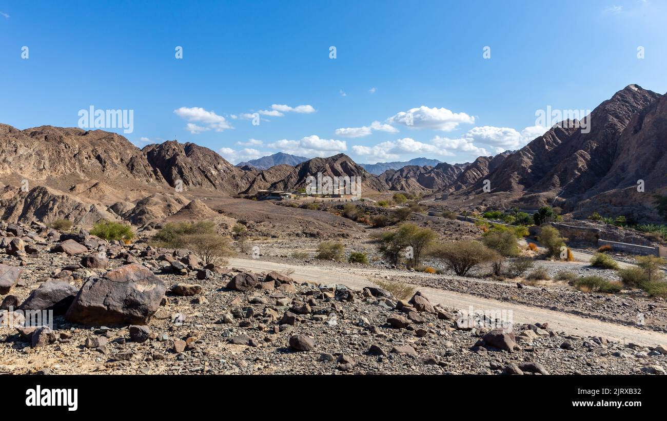 Landscape view of Wadi Shawka  dry riverbed with Emirates Adventures camp buildings, rocky Hajar Mountains in the background, United Arab Emirates. Stock Photo