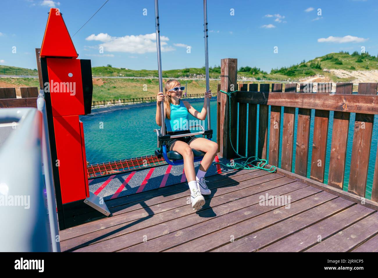 Girl arrives on a skydive chair in a mountain adventure park. Lake in background Stock Photo