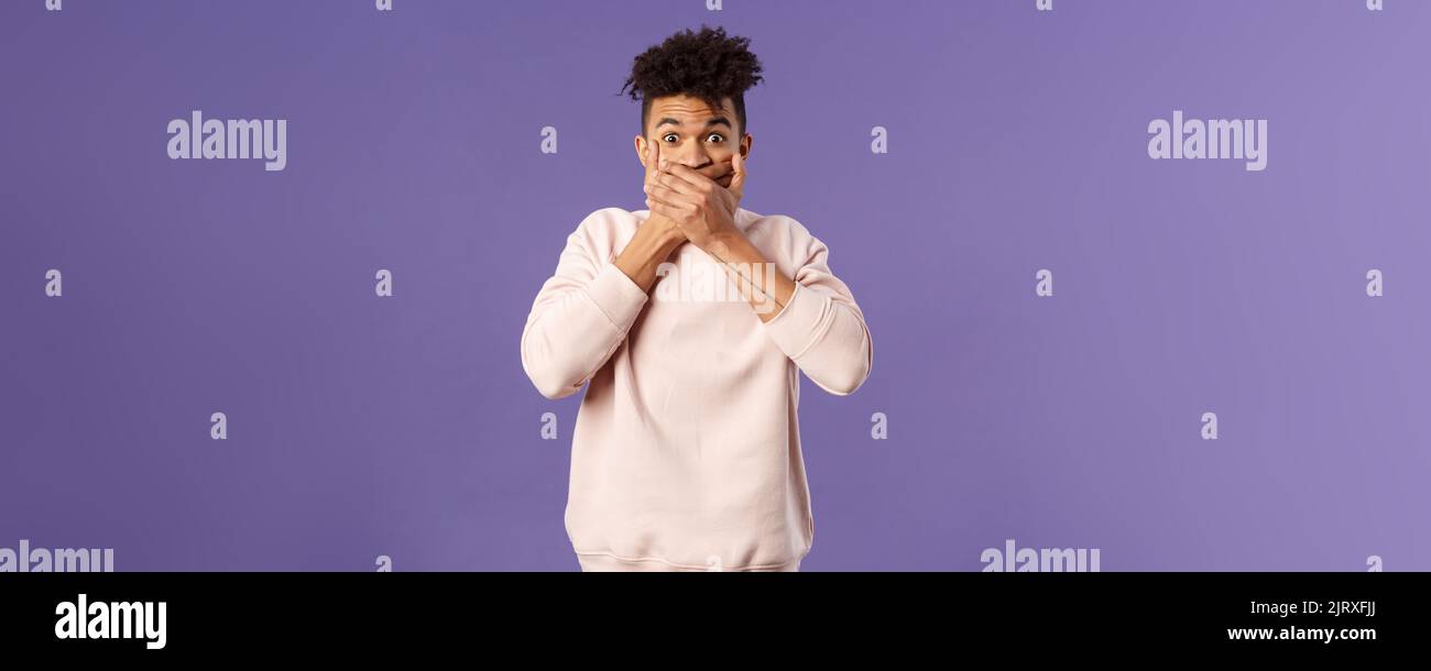 Portrait of shocked impressed young hispanic man found out gossip, heard rumour, trying not laugh shut his mouth with hands and express amazement and Stock Photo