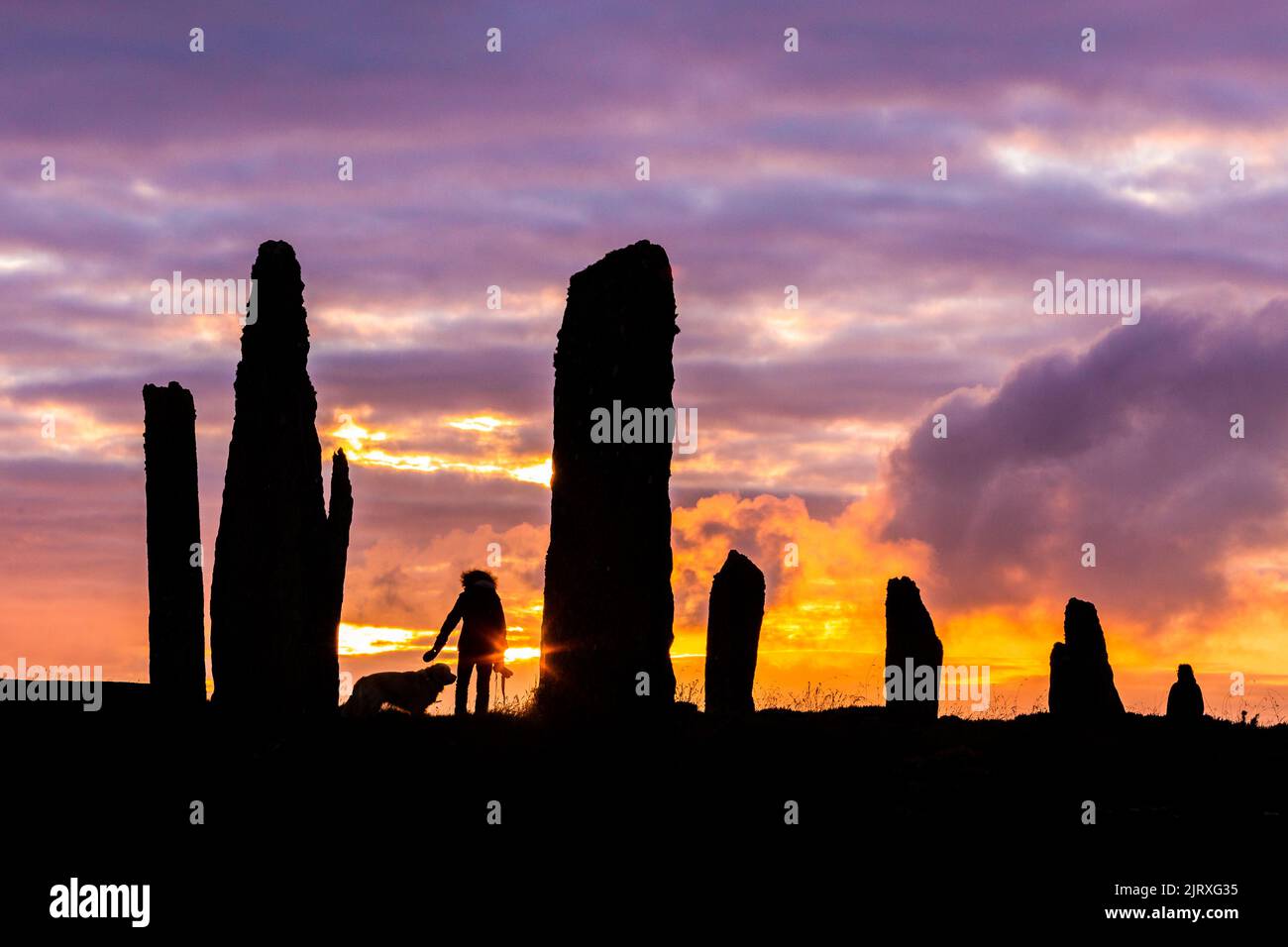 Orkney, UK. 26th Aug, 2022. A woman walks her dog as the sun sets at the Ring of Brodgar, Orkney. The 5,000 year old massive stones are part of the Heart of Neolithic Orkney World Heritage Site. Credit: Peter Lopeman/Alamy Live News Stock Photo