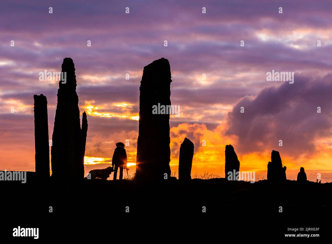 Orkney, UK. 26th Aug, 2022. A woman walks her dog as the sun sets at the Ring of Brodgar, Orkney. The 5,000 year old massive stones are part of the Heart of Neolithic Orkney World Heritage Site. Credit: Peter Lopeman/Alamy Live News Stock Photo