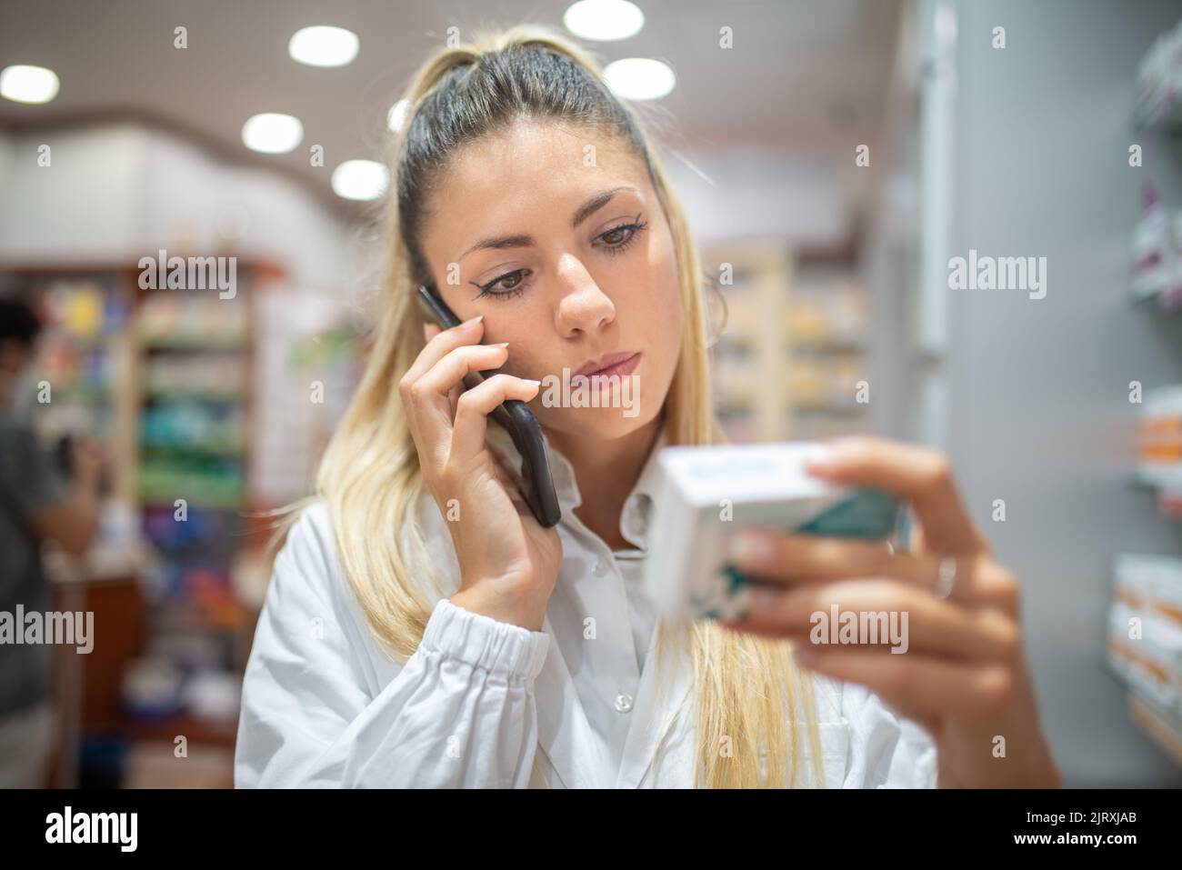 Pharmacist checking drug in a pharmacy while talking on the phone Stock Photo