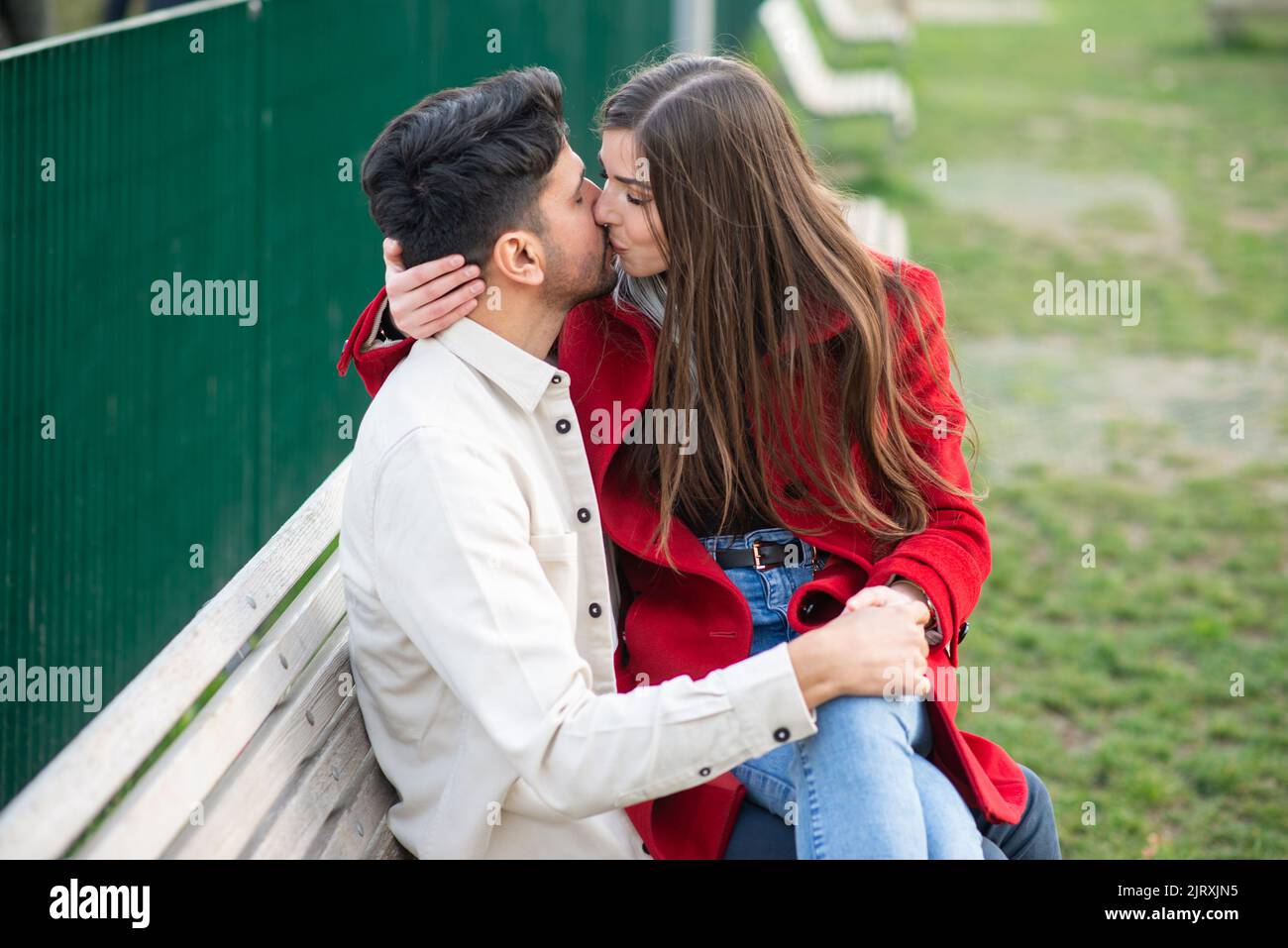 Happy couple sitting on a bench outdoors and kissing Stock Photo - Alamy