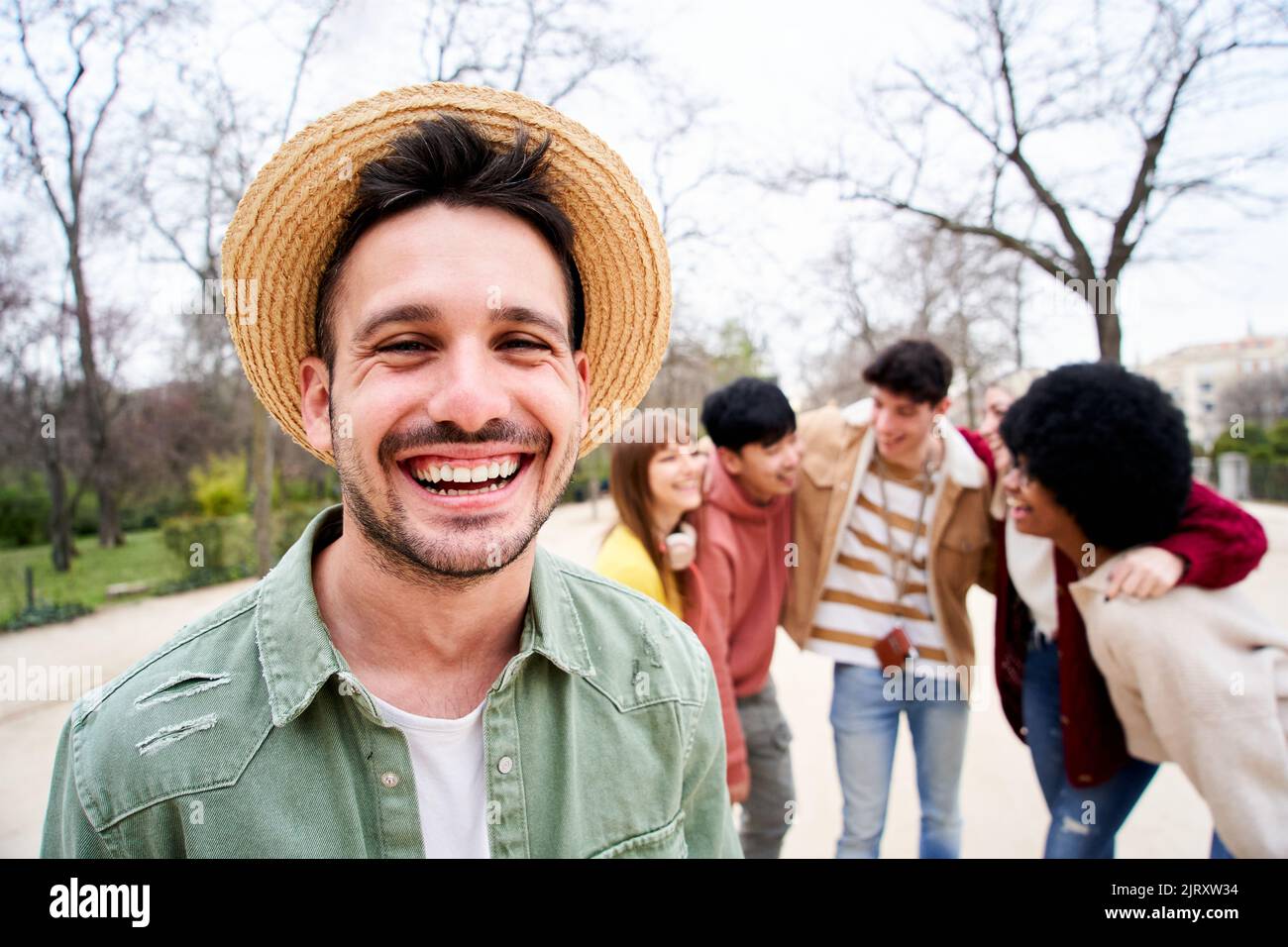 Young smiling guy looking at the camera outdoors with group of friends