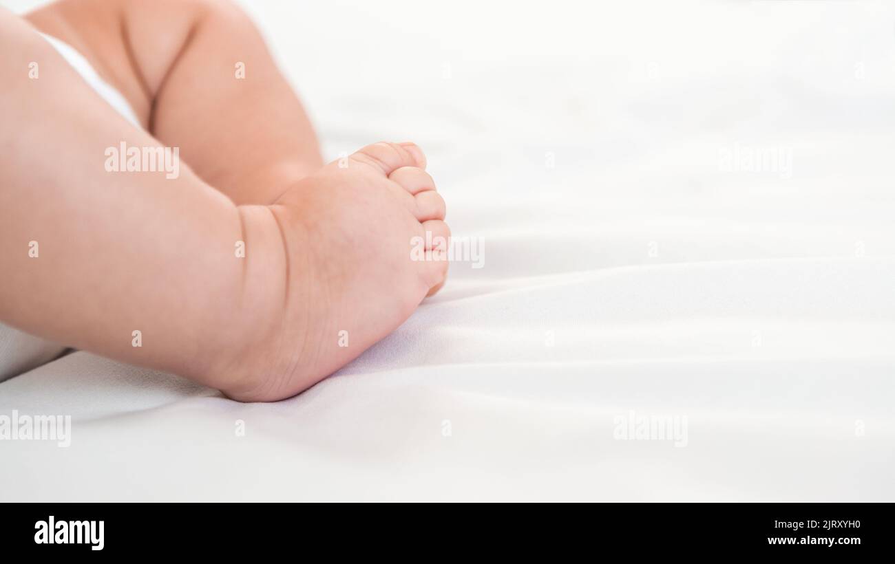 A chubby foot of little baby on white sheet background. Cute newborn age of 3 months. Boy sleeping on the mother's bed. Family maternity concept Stock Photo