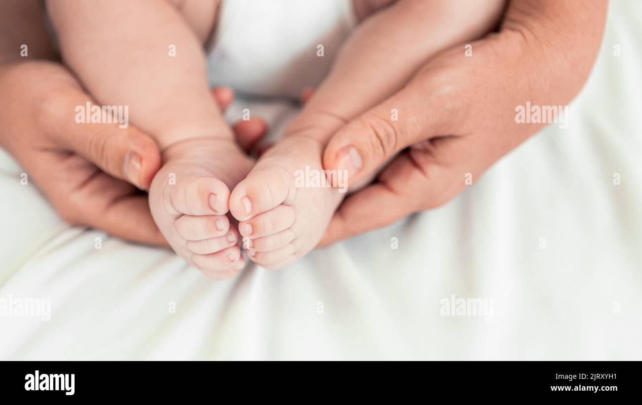 Close up mom hands holding foots baby in a room with a lot of sunlight. The newborn sleeping on the mother's bed. Health care, love and relationship c Stock Photo