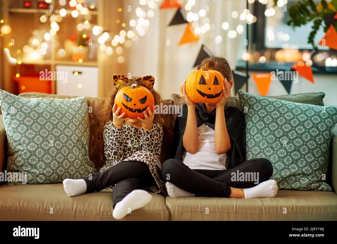 girls in halloween costumes with pumpkins at home Stock Photo