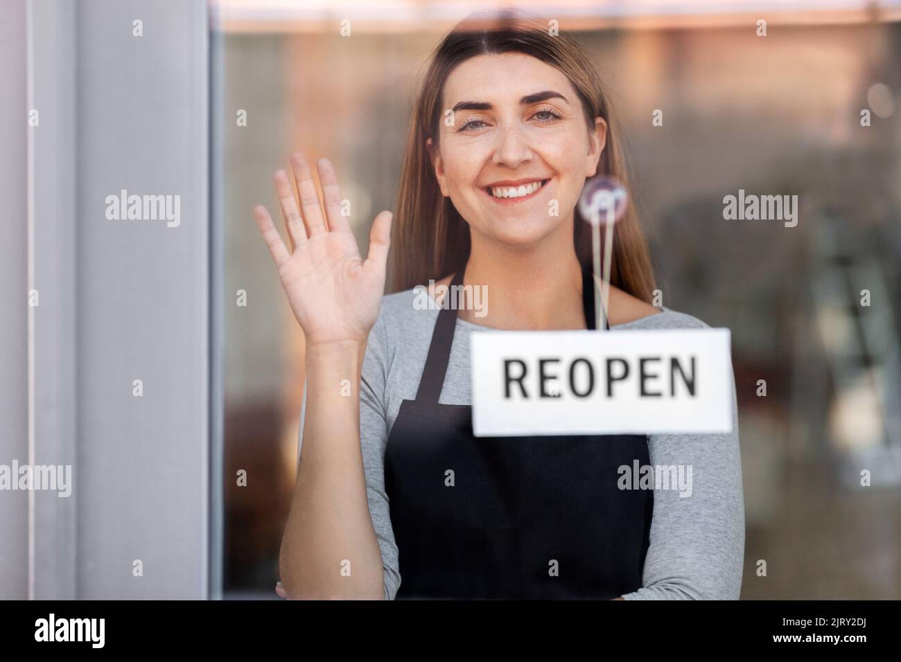 happy woman hanging reopen banner to door glass Stock Photo