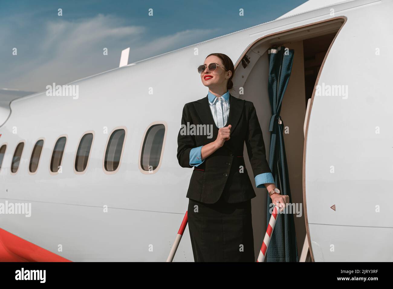 Woman flight attendant in sunglasses standing on airplane stairs at