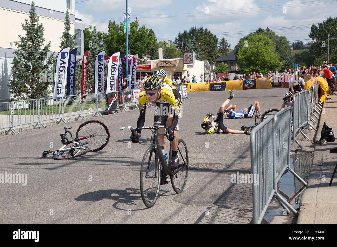 Two bicycle racers lying in the street after falling at 'crash corner' on the Tour de Bowness criterium, an urban cycling road race in Calgary, Canada Stock Photo