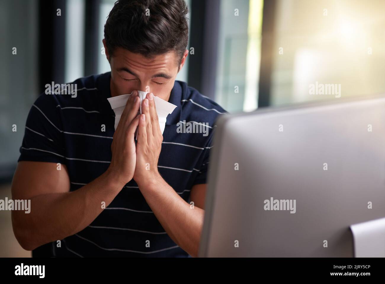 Sick and stuck at work. a young businessman blowing his nose in an