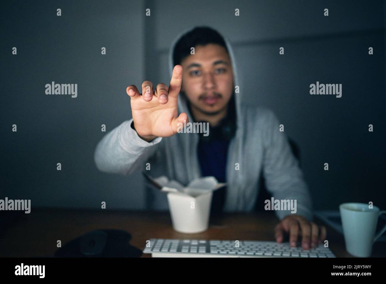 Touching the future. a young man using an unseen digital interface while sitting at a computer late at night. Stock Photo