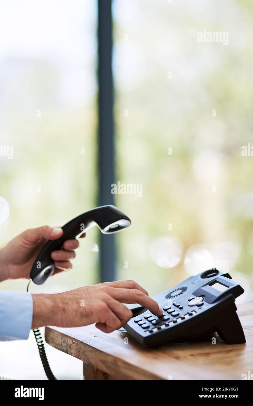Opening up the lines of communication. a man dialing a number on a telephone at work Stock Photo