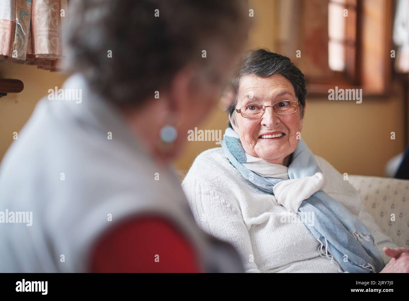 Happy elderly woman talking to friend sitting on sofa in retirement home having conversation Stock Photo