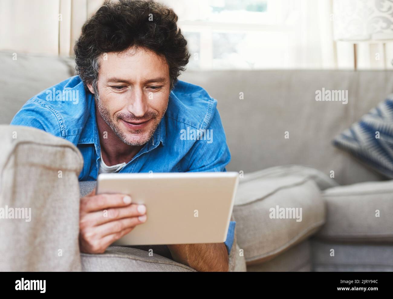 Seeing the world from the comfort of his couch. a bachelor relaxing on the sofa with his tablet. Stock Photo