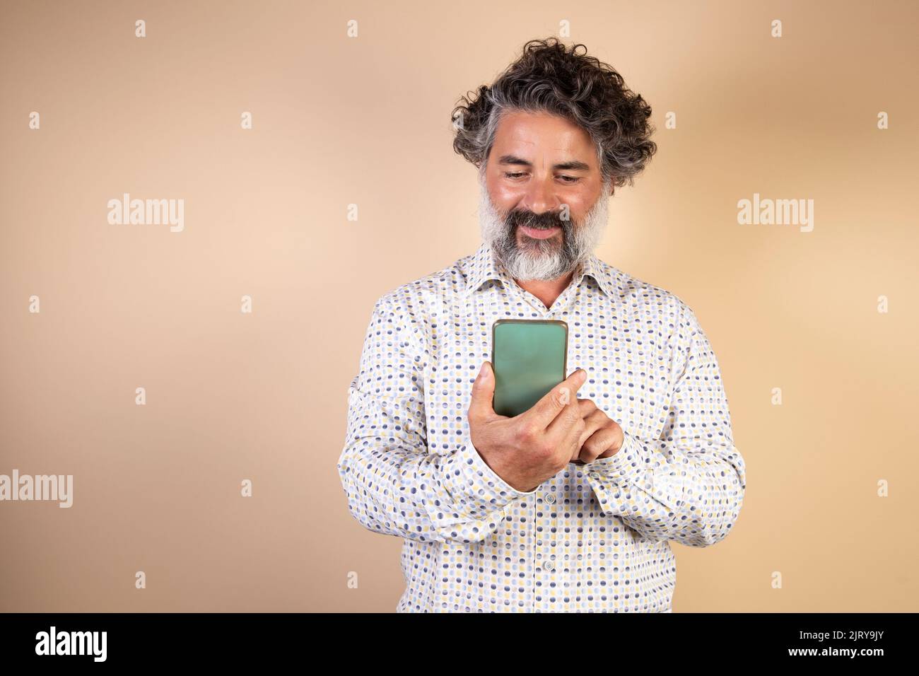 An average adult sends phone messages on a smart phone. Smiling modern man using smartphone on light wall. Happy man using app on mobile phone. Stock Photo