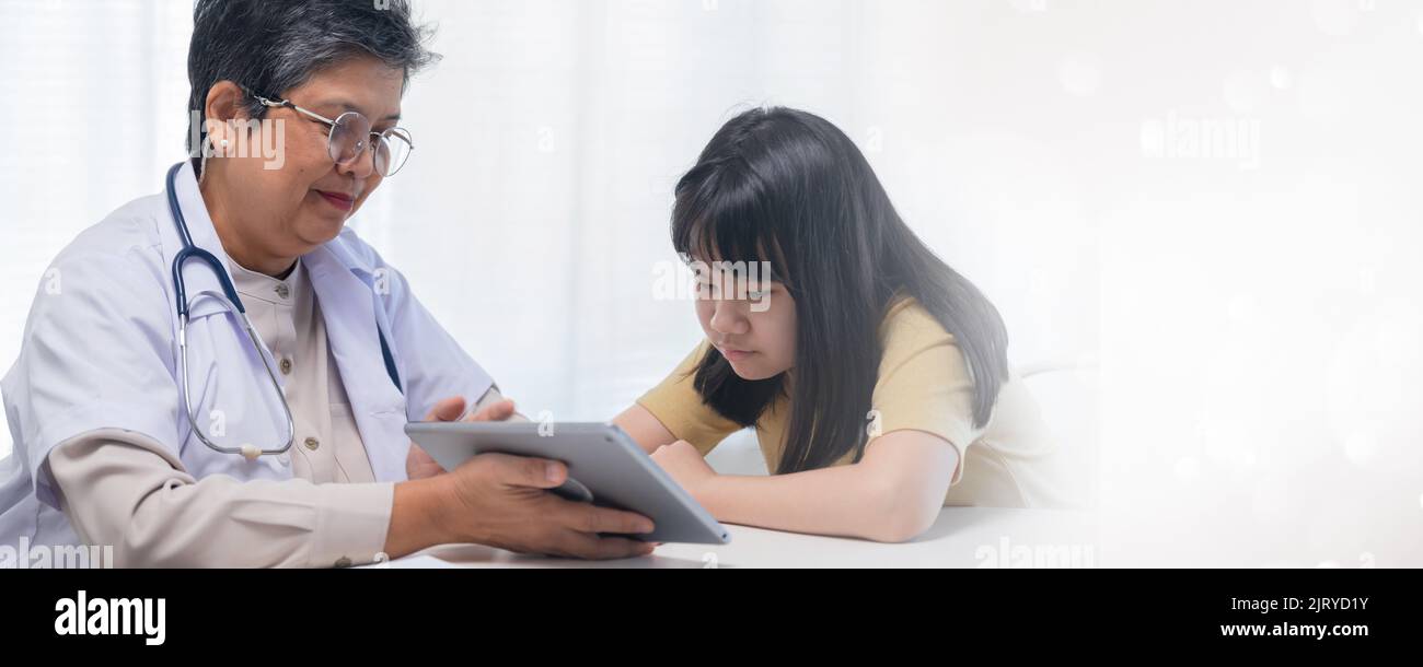 Elder woman doctor talk and show tablet for young girl looking at and explaining before treatment Stock Photo