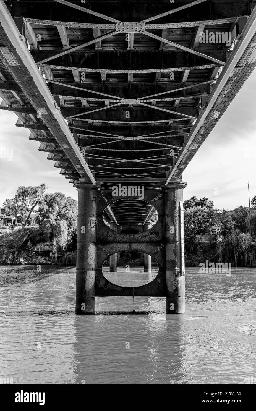 A monochrome vertical shot of the base of an old bridge over water with trees in the background Stock Photo