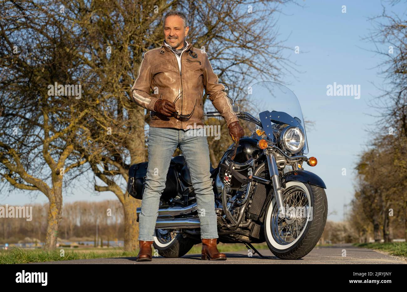 Middle-aged man with leather jacket standing in front of his motorbike and holding sunglasses, Karlsruhe, Germany Stock Photo