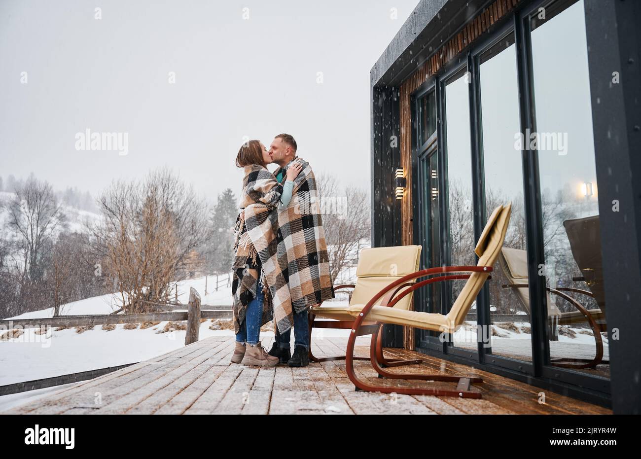 Man and woman wrapped in blanket kissing outdoors under winter snow