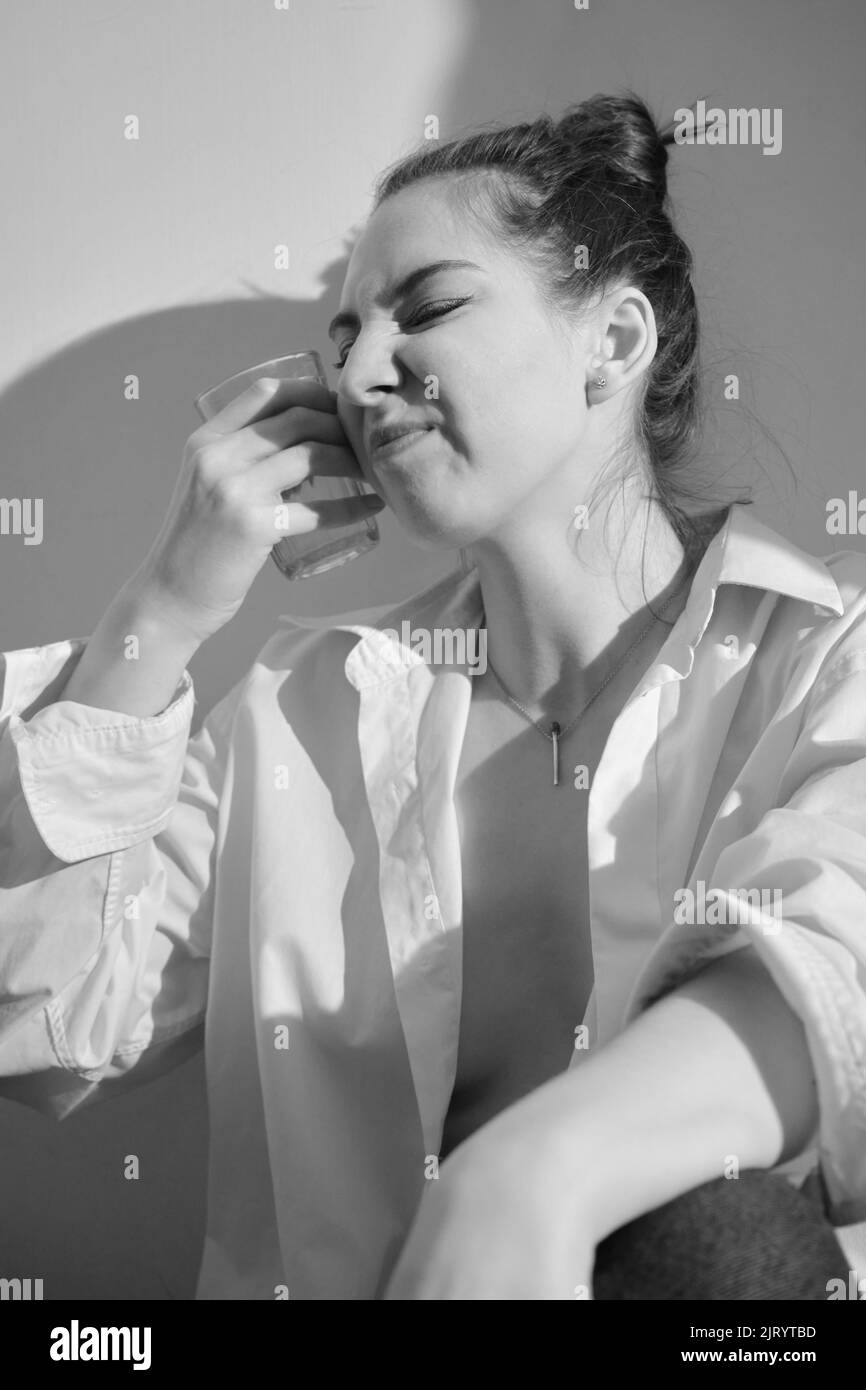 Young woman drinking alcohol from glass against sunny wall background