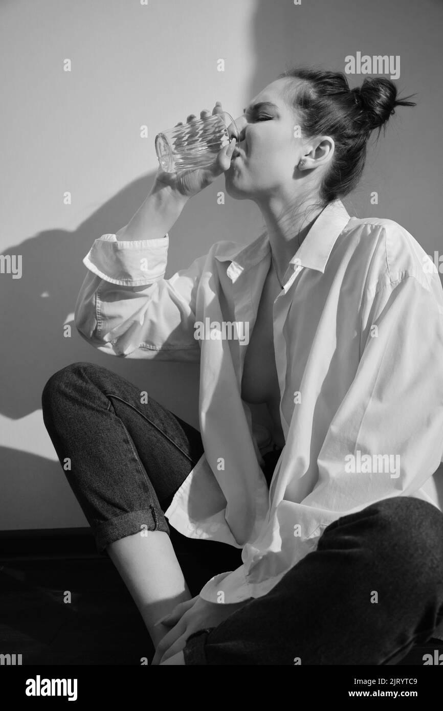 Young woman drinking alcohol from glass against sunny wall background