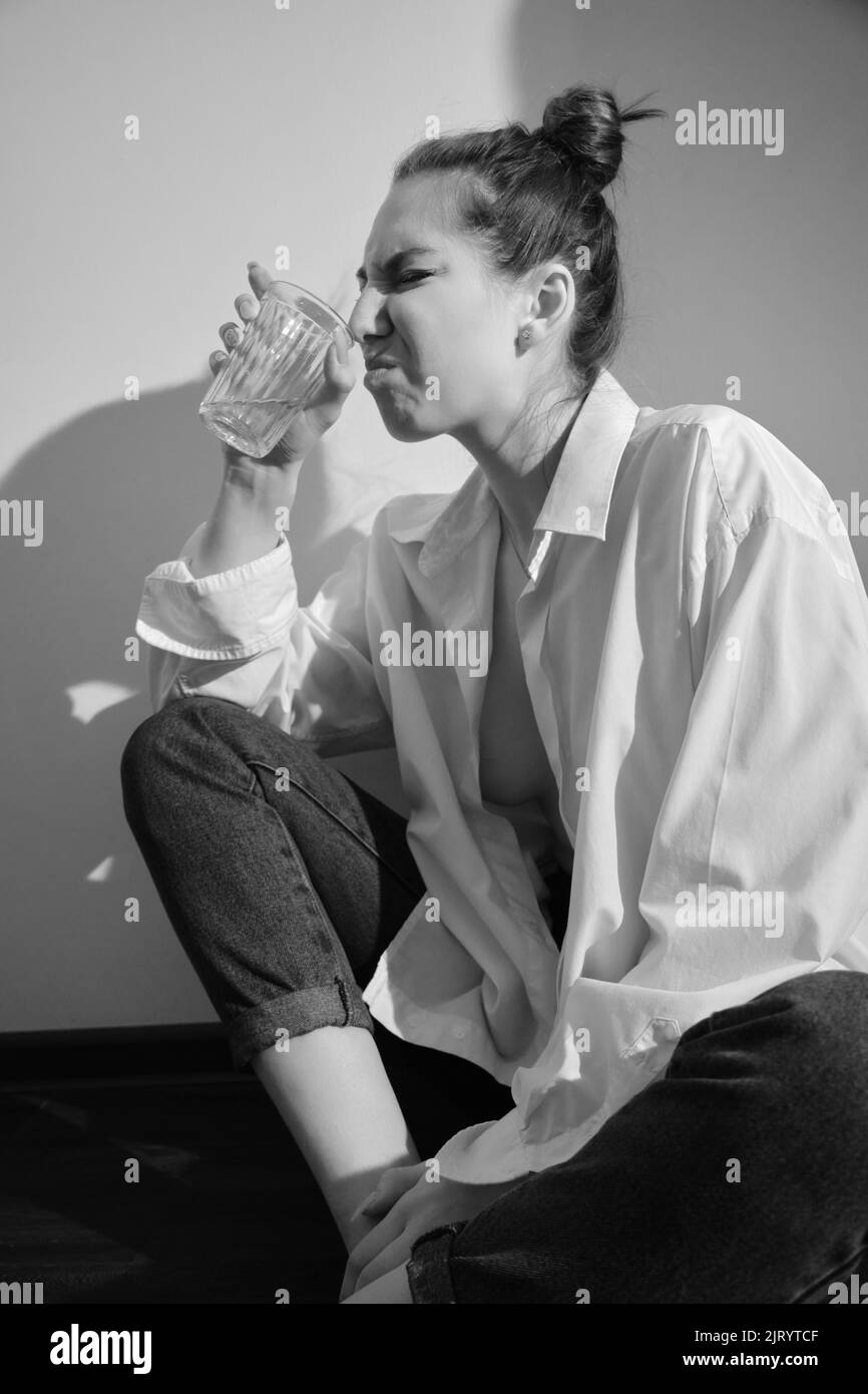Young woman drinking alcohol from glass against sunny wall background