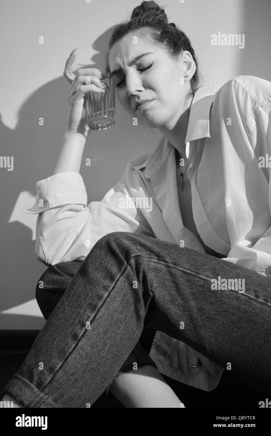 Young woman drinking alcohol from glass against sunny wall background