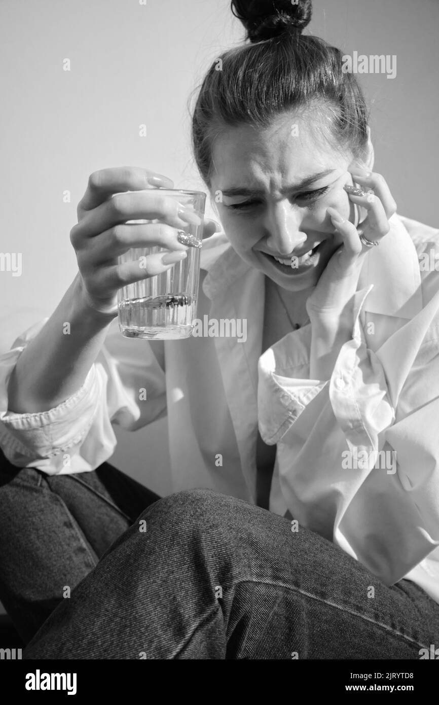 Young woman drinking alcohol from glass against sunny wall background