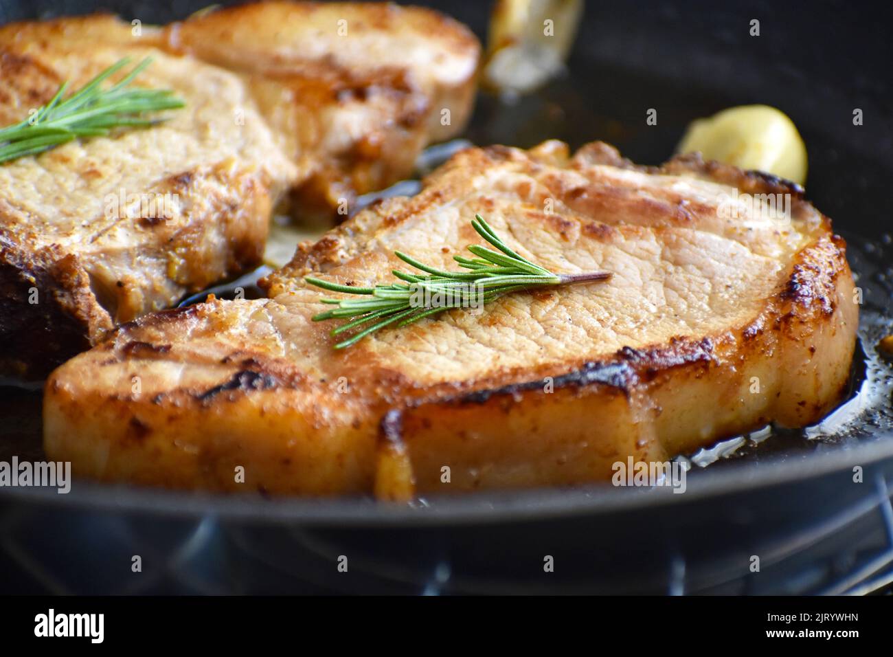 Pork chop on a frying pan. Grilled pork steak with garlic and rosemary on a black metal pan. Stock Photo