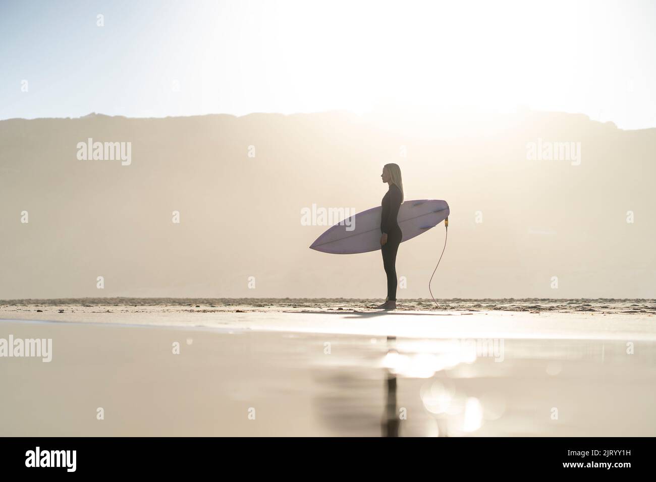 Beautiful surfer girl at the beach standing with her surfboard at sunset time. Female surfer Stock Photo