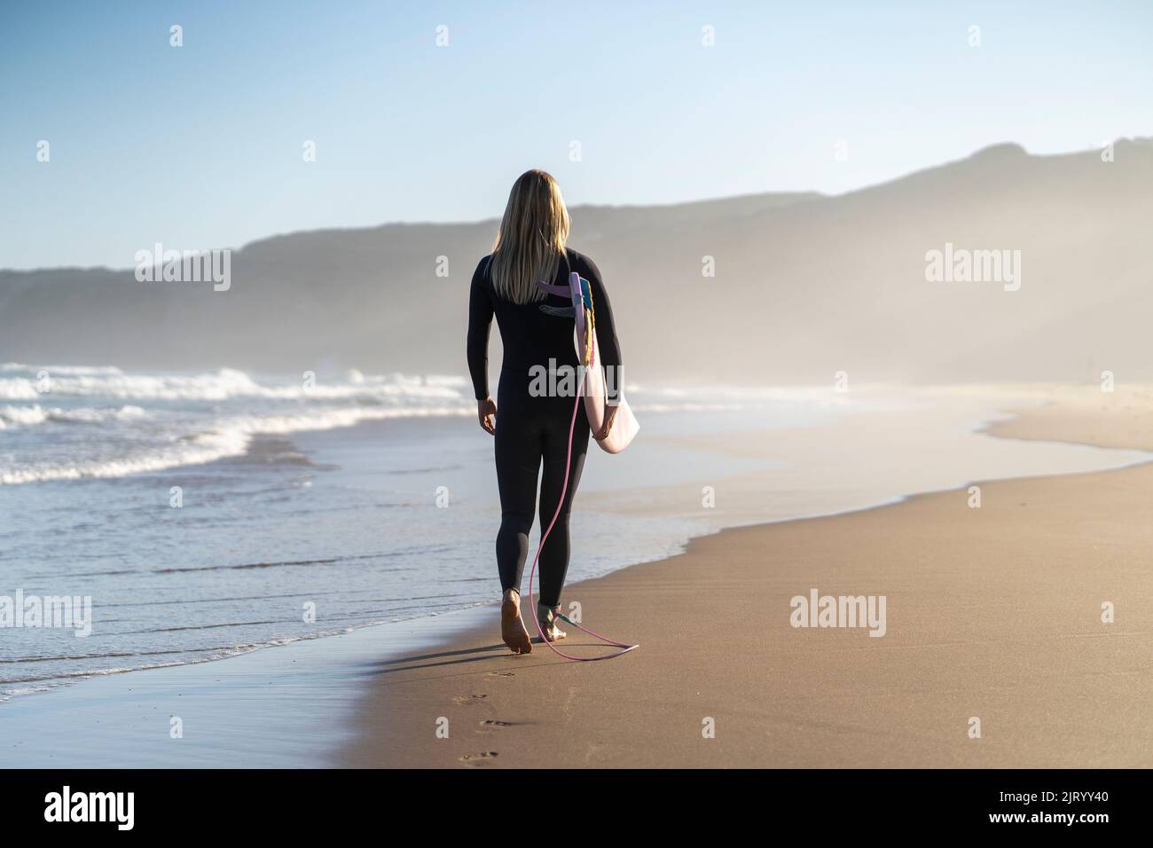 Surfer girl at the beach walking with her surfboard in the morning. Female surfer woman Stock Photo