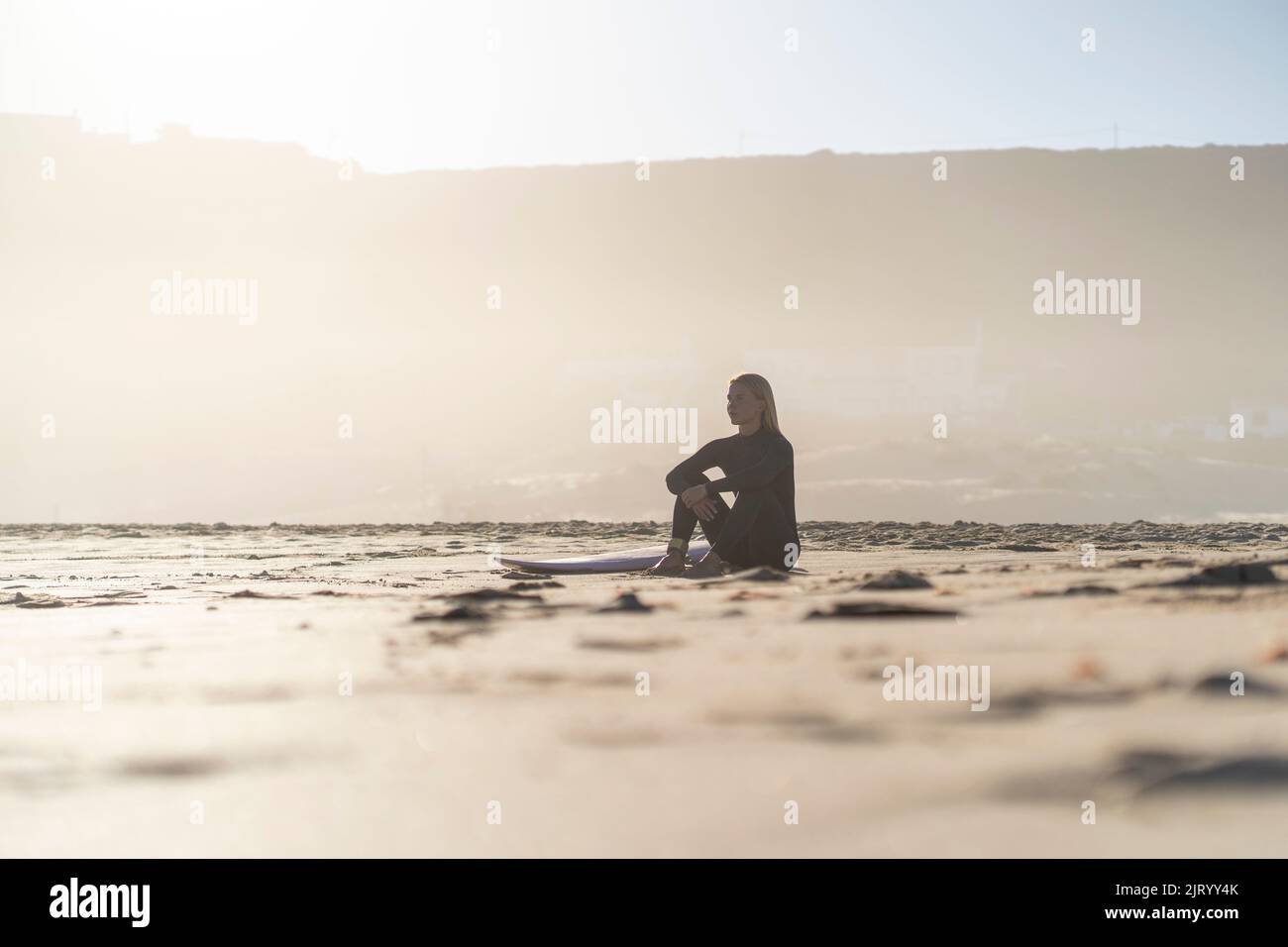 Young woman with surfboard sitting on beach at sunset hi-res stock ...