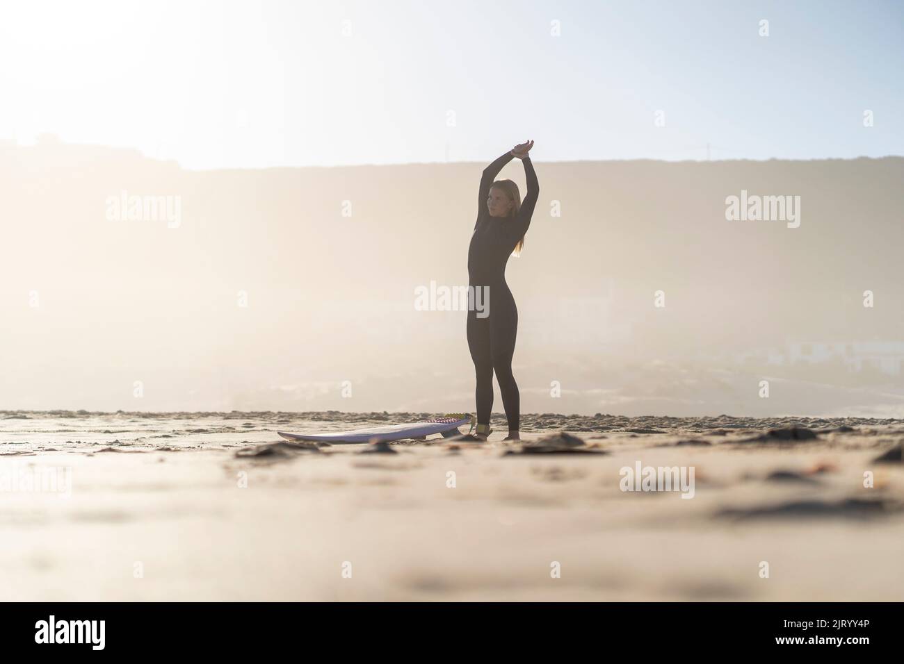 Surfer at the beach. Surfer girl warming up with surfboard on the beach. Morning light beautiful sunrise colors. Stock Photo