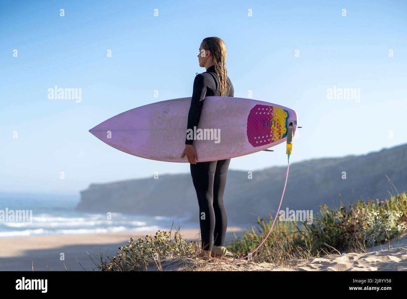 Surfer girl at the beach with her surfboard looking at the waves in the morning. Stock Photo
