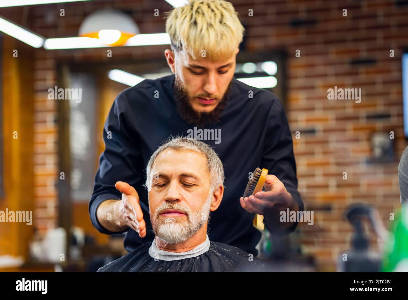trendy stylish master cuts hair of old man client in modern barbershop Stock Photo