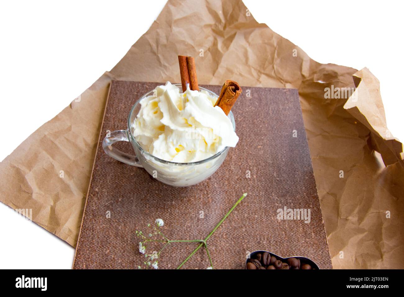 branch of flowers, heart form coffee beans, cinnamon sticks, whipped cream in a glass cup composition in brown tones on crumpled wrapping paper Stock Photo