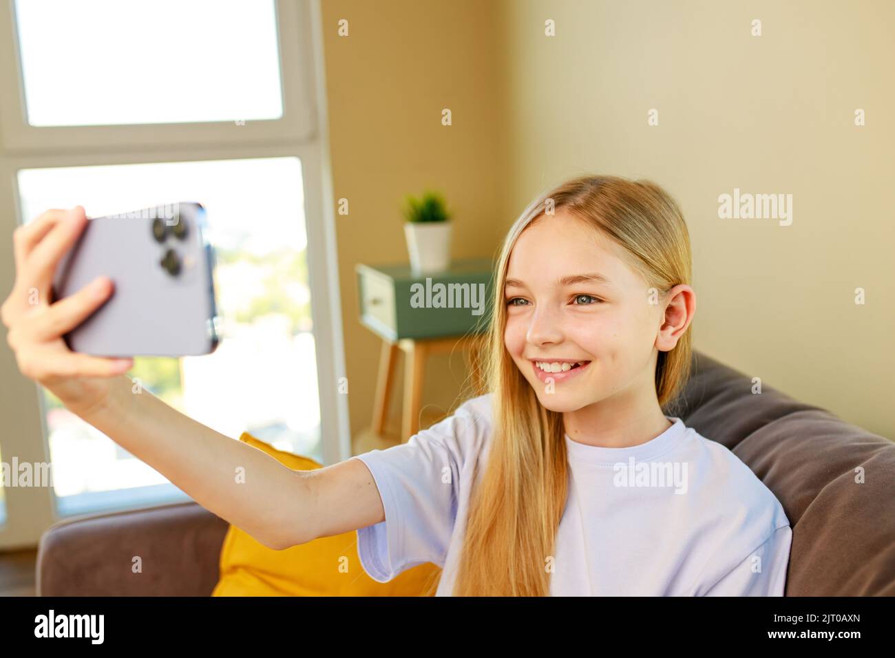 pre-teen girl making selfie photos on her smartphone in cozy living room at home Stock Photo