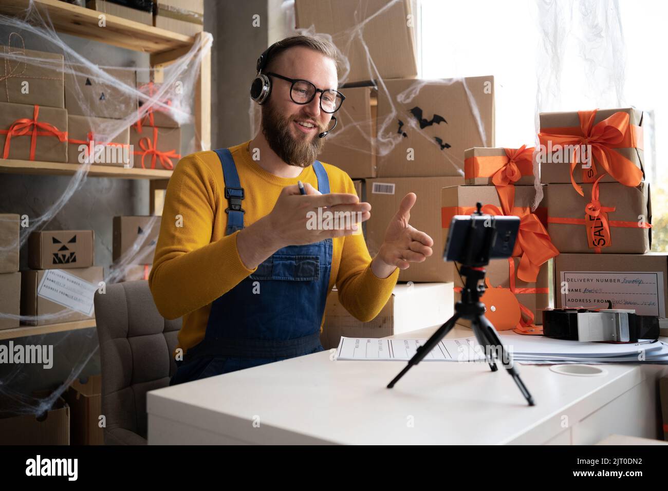 bearded man in glasses business owner sits in halloween decorated home office. takes orders online via video call. selling goods for the holiday of Stock Photo