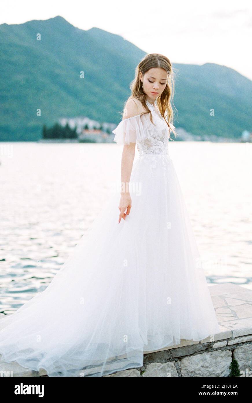 Bride in a white dress stands on a tiled border by the sea Stock Photo ...