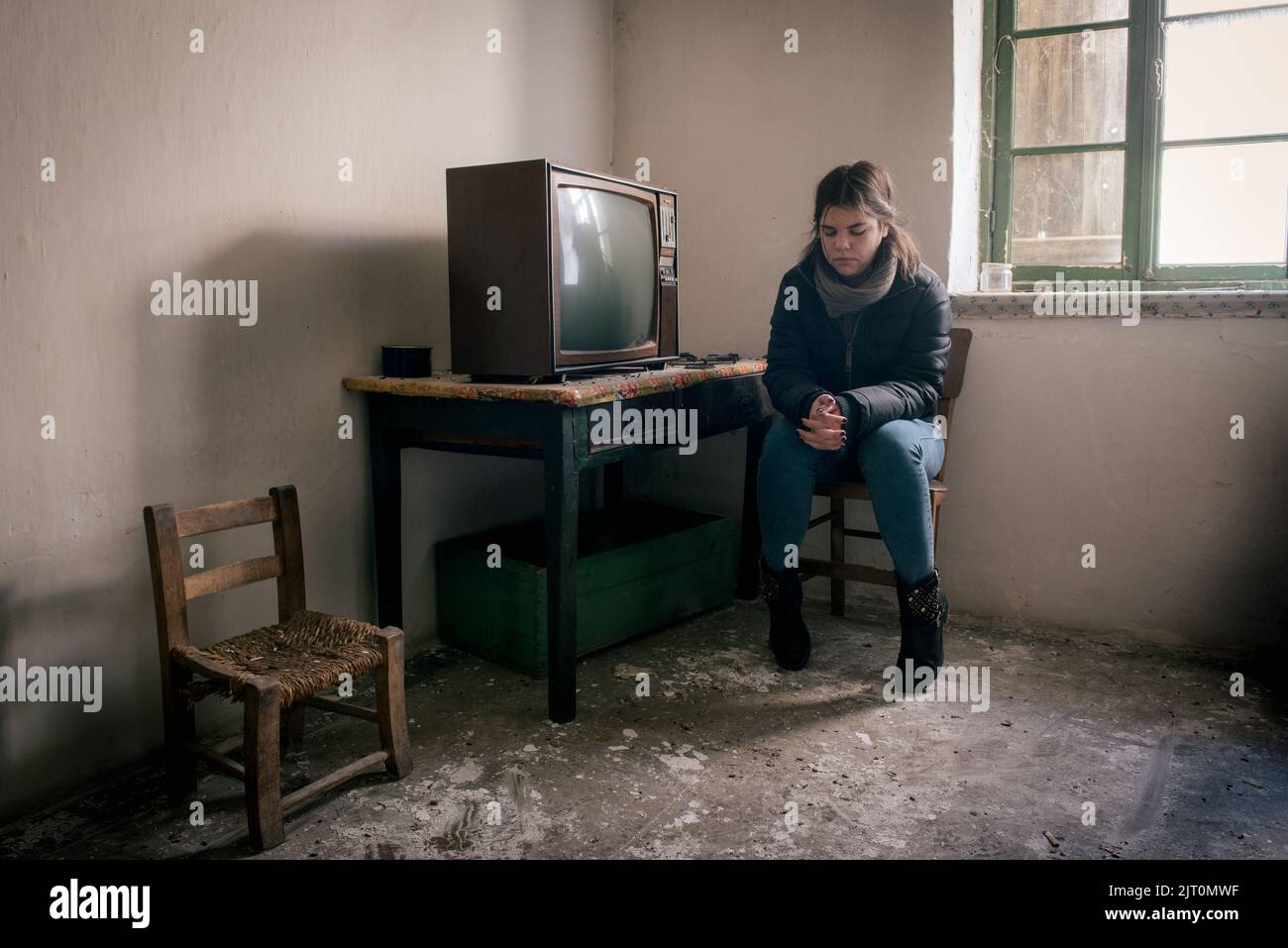 Young woman lonely in an abandoned ruined room with television. Loneliness concept Stock Photo