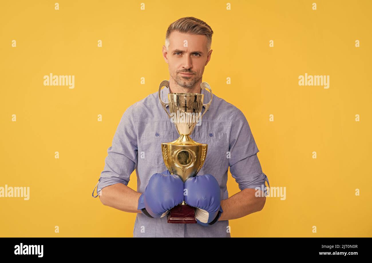 mature man in boxing gloves hold champion cup on yellow background, success Stock Photo