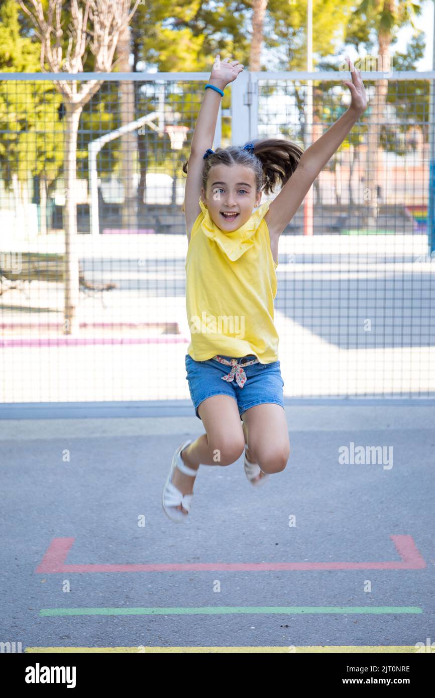 A happy young girl springing in the playground with the park in the background Stock Photo
