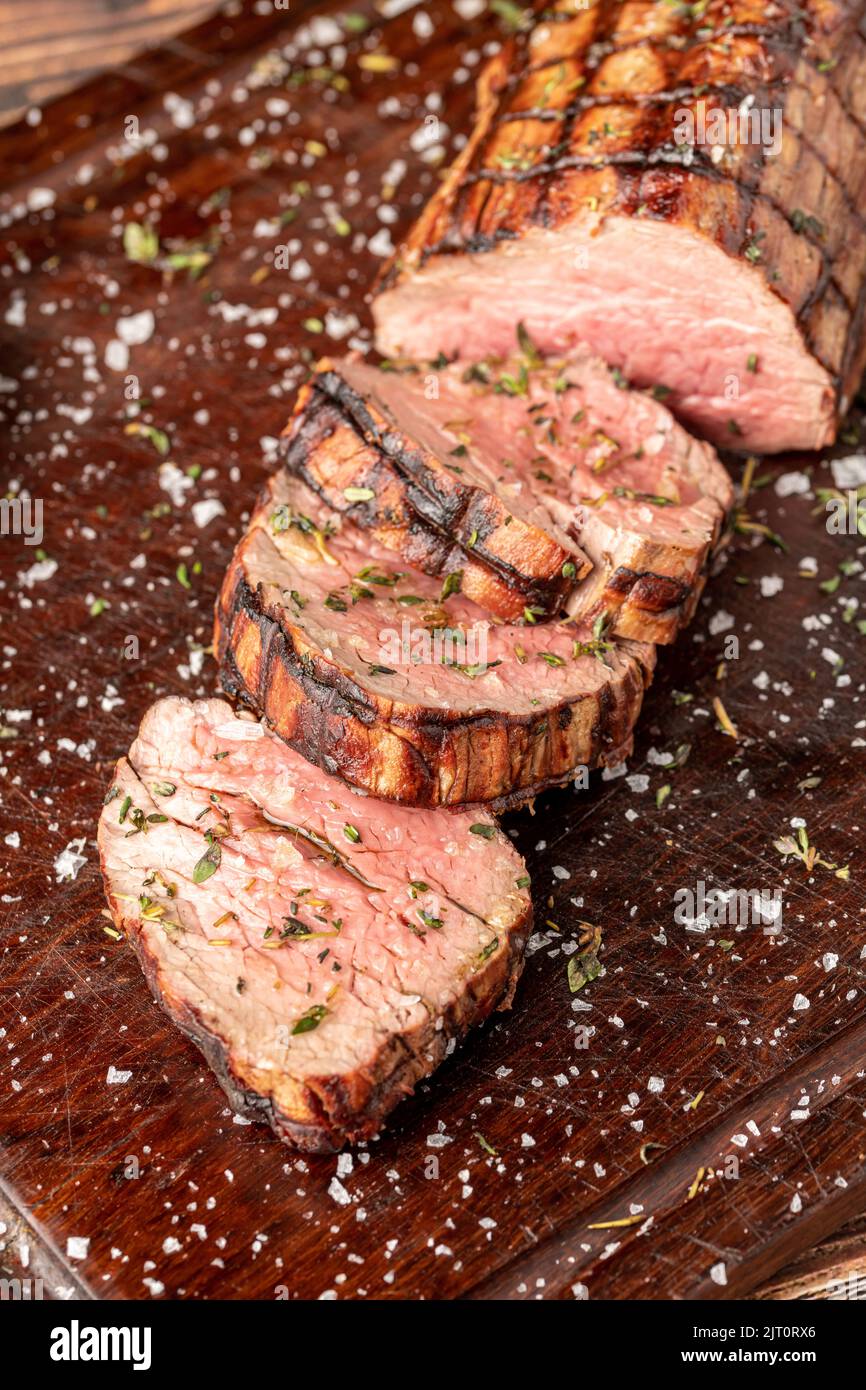 Sliced grilled beef tenderloin seasoned with salt, rosemary and thyme on a wooden cutting board Stock Photo