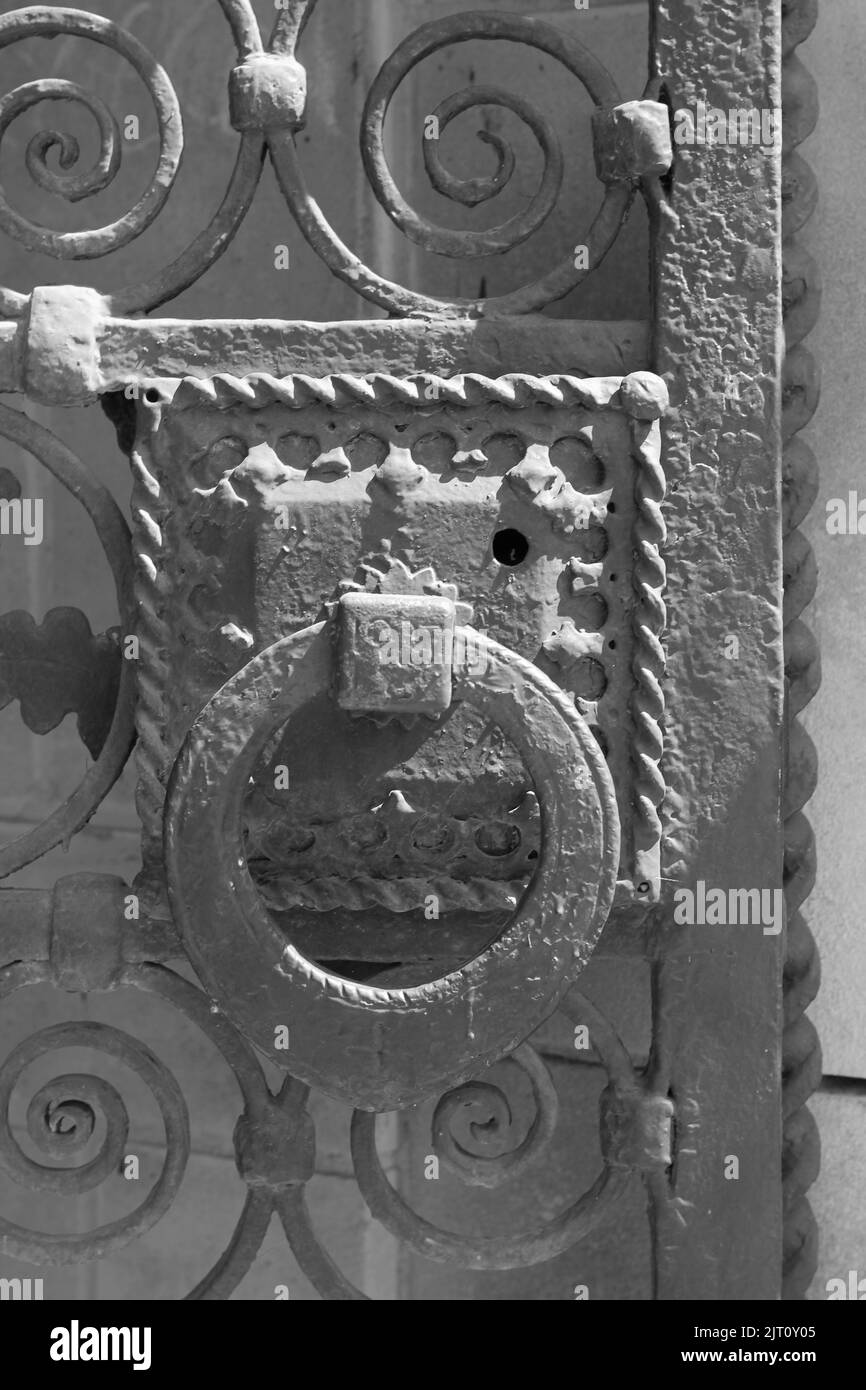Huge heavy door knocker on a cast iron metal gate wall in a black and