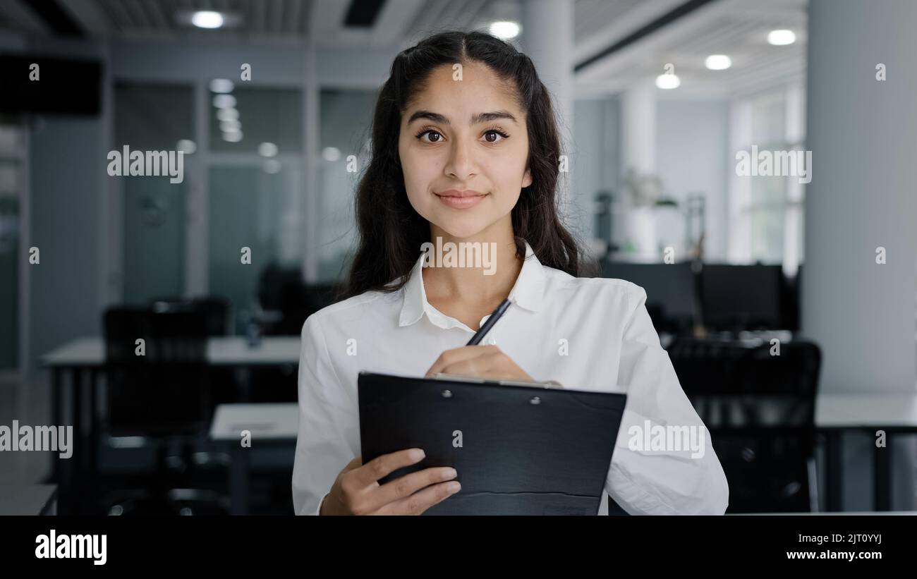 Young woman secretary writes down details of task writing data in clipboard makes daily appointments cute girl trainee listens to supervisor takes Stock Photo